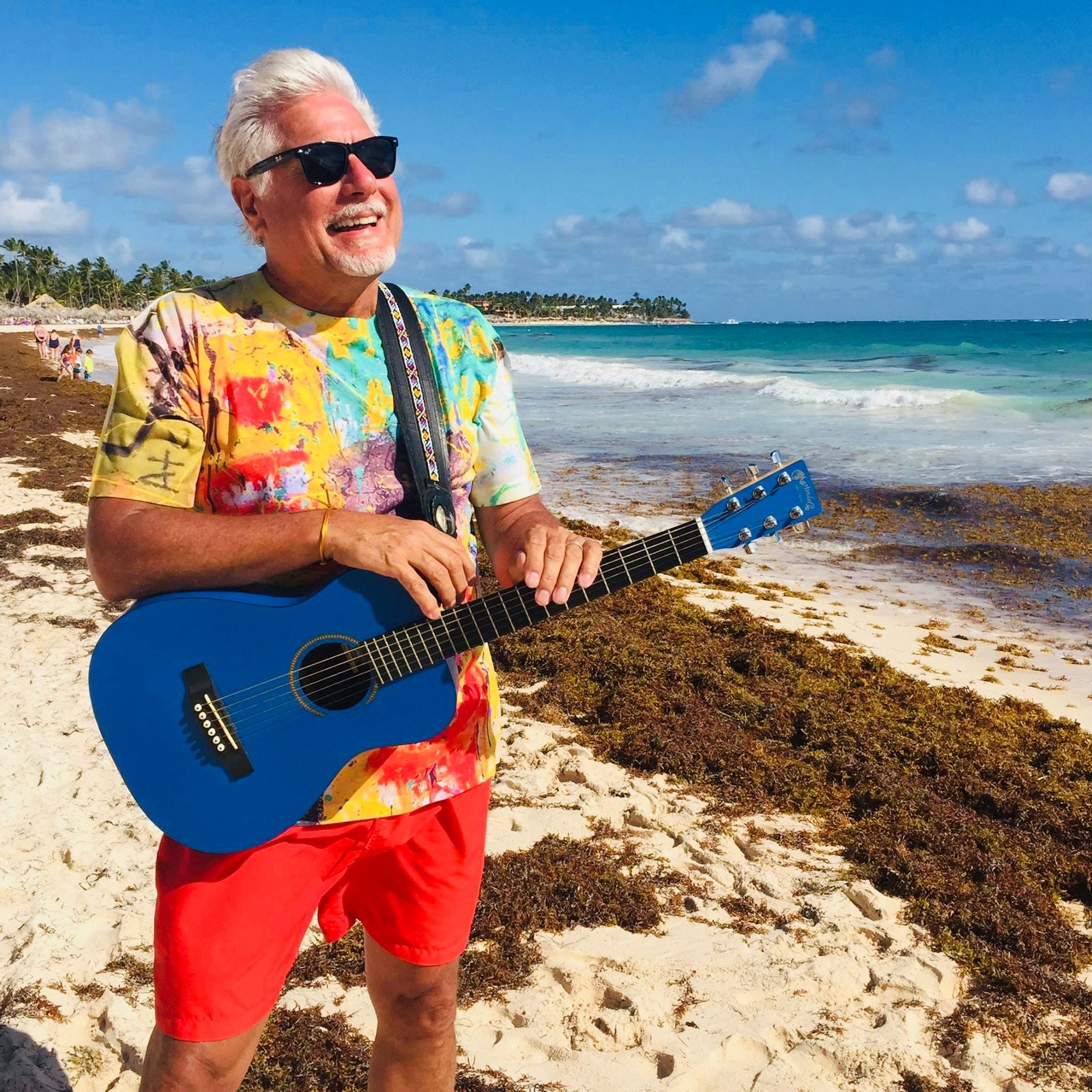 Robert Dempster laughing on a sunny beach with a bright blue acoustic guitar