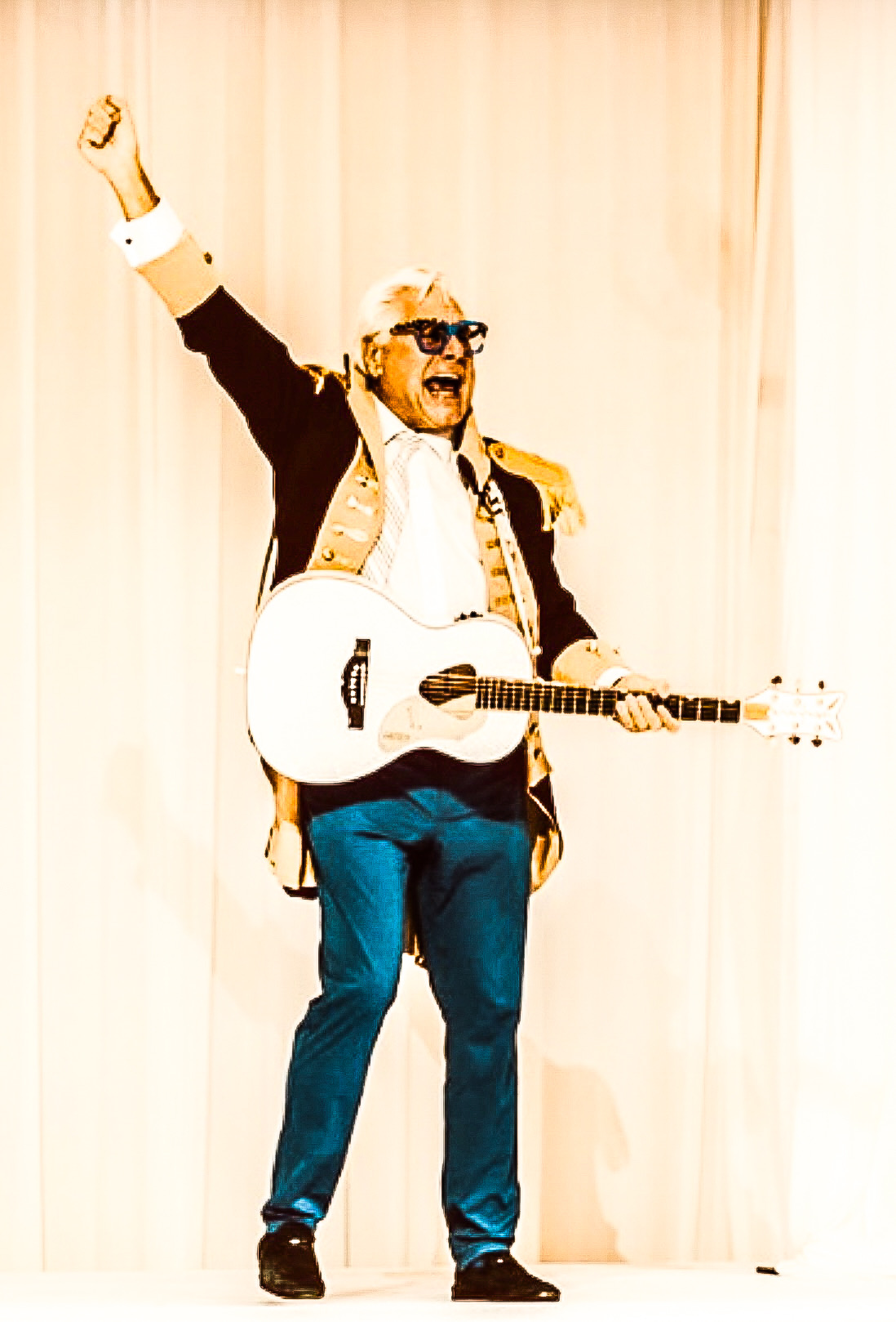 Robert Dempster on stage with a fist raised, holding a white guitar
